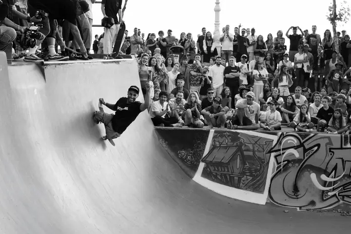 Skater subiendo por la pared de un bowl ante un público que lo mira y aplaude, en blanco y negro