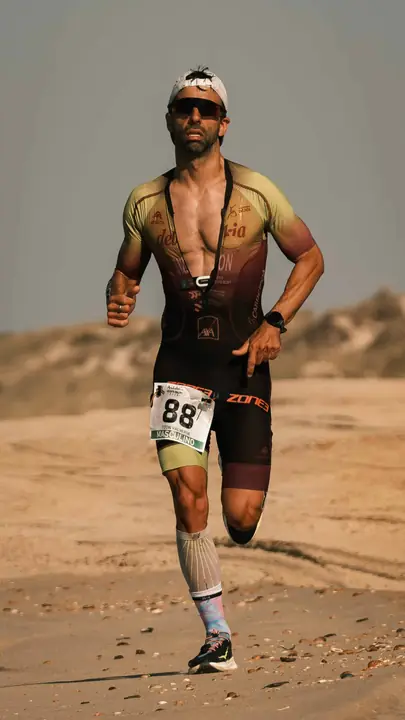Triatleta corriendo por una playa de arena, con dorsal y gafas de sol