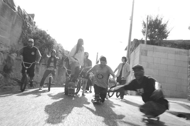 Grupo de ciclistas de BMX y patinadores bajando una cuesta, con movimiento, en blanco y negro