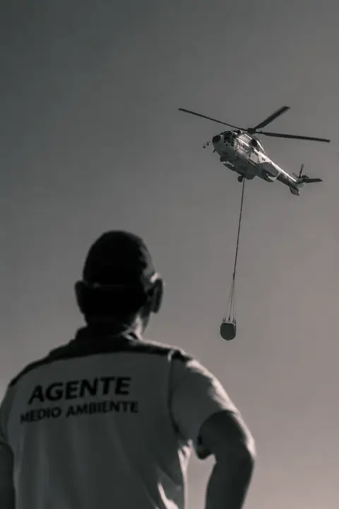 Agente de Medio Ambiente mirando un helicóptero con helibucket, en blanco y negro