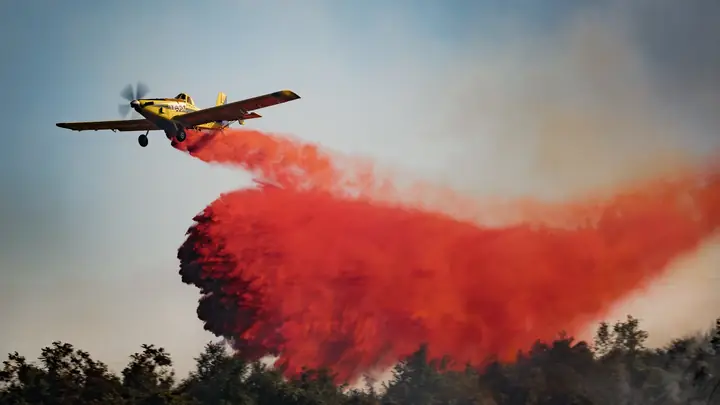 Avioneta soltando retardante rojo sobre el bosque