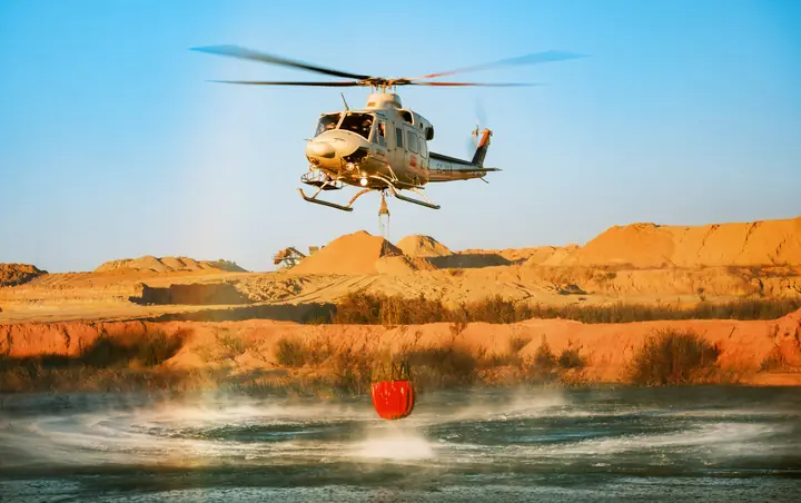 Helicóptero cargando agua en una cantera al atardecer