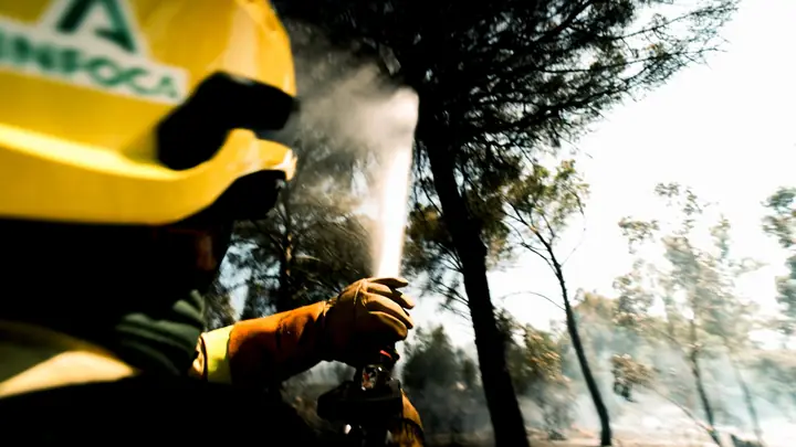 Bombero forestal en primer plano con casco INFOCA y chorro de agua