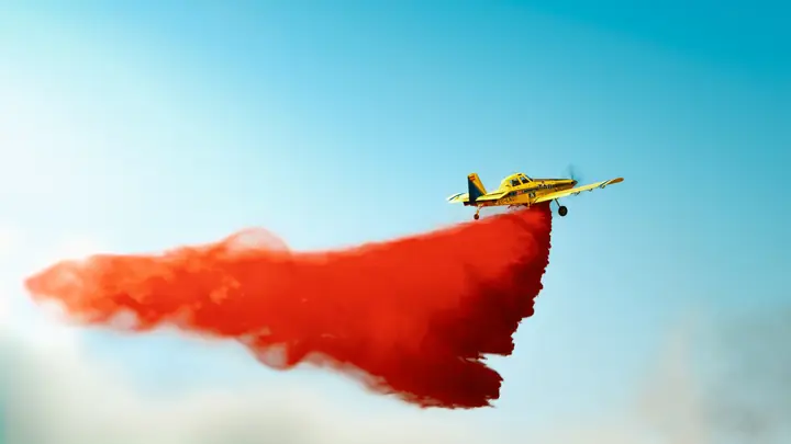 Avioneta TA8 con una gran estela de retardante rojo sobre cielo azul