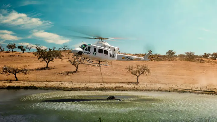 Helicóptero blanco cargando agua en un embalse de dehesa
