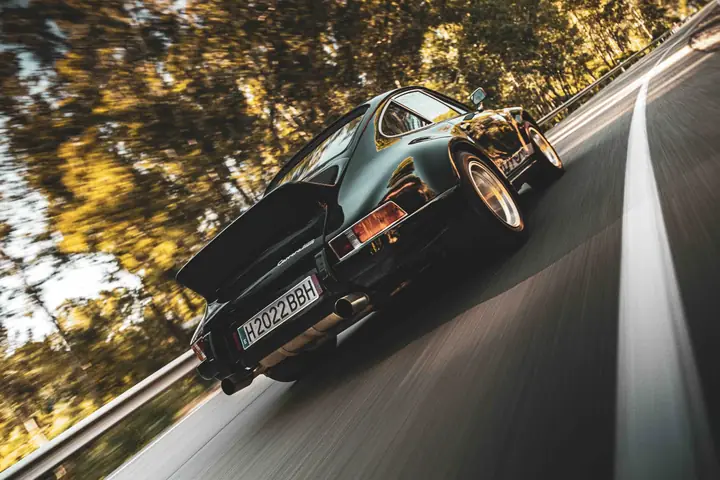 Porsche 911 clásico negro visto desde atrás en una carretera de bosque, con barrido