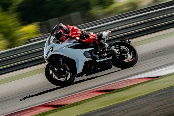 Moto deportiva plateada y piloto de rojo inclinados en curva, con barrido