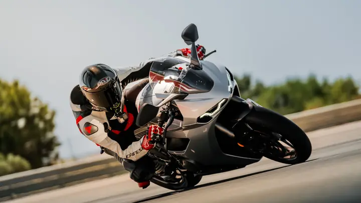 Piloto y moto plateada inclinados al máximo en una curva